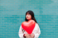 Beautiful Woman Looking Away Holding Heart Shape Balloon In Front Of Turquoise Wall