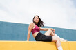 © VISTA by Westend61 - Woman in sports clothing looking away while sitting on yellow wall