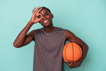 Wall Mural - Young African American man playing basketball isolated on blue background excited keeping ok gesture on eye.