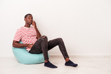 Young African American man sitting on a puff isolated on white background biting fingernails, nervous and very anxious.