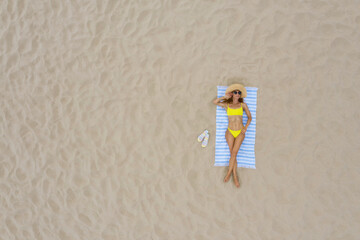 Canvas Print - Woman sunbathing on beach towel at sandy coast, aerial view. Space for text