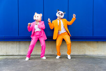 Man And Woman Wearing Vibrant Suits And Bear Masks Dancing Side By Side Against Blue Wall