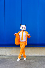 Man Wearing Vibrant Orange Suit And Panda Mask Standing Confidently Against Blue Wall