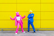 © VISTA by Westend61 - Man and woman wearing vibrant suits and animal masks posing together in front of yellow wall