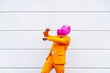 © VISTA by Westend61 - Man wearing vibrant orange suit and hippo mask dancing in front of white wall