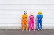 © VISTA by Westend61 - Three people wearing vibrant suits and animal masks posing side by side in front of white wall