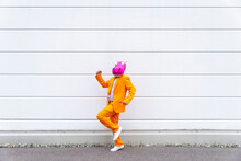 Man Wearing Vibrant Orange Suit And Hippo Mask Jogging In Front Of White Wall