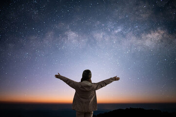 Wall Mural - Silhouette of young woman traveler and backpacker standing and watched the star and milky way alone on top of the mountain. She enjoyed traveling and was successful when he reached the summit.