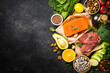 Keto diet food. Healthy food products at black background. Salmon steak, beef, beans, nuts, vegetables and olive oil. Top view image at black stone table.