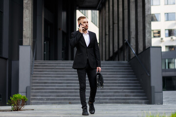 Wall Mural - A Banker In A Stylish Suit With A Cell Phone And A Briefcase In His Hand Goes Down The Stairs On The Street To Meet With Investors. Business Concept Photo