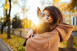 Close up portrait of a caucasian woman with long brunette hair holding her adorable yorkie, standing in front of the sunlight. Golden hour, fall season.