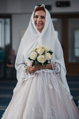 Poster - Vertical shot of the red-haired bride walking to the altar in a veil holding her bouquet