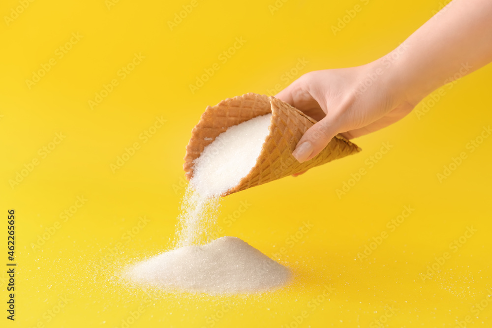 Woman sprinkling sugar from waffle cone on color background