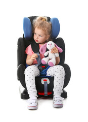 Canvas Print - Cute little girl with toy buckled in car safety seat on white background