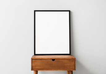 blank poster frame on wooden table near light wall