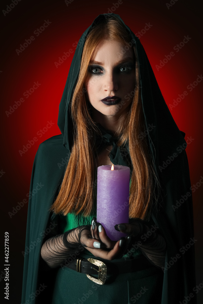 Young witch with candle on dark background