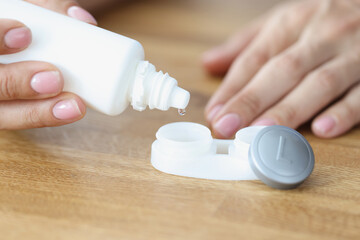 Poster - Woman drips lens solution into box closeup