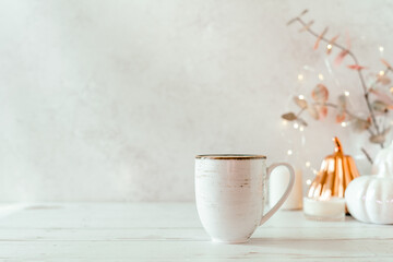 Details of Still life, cup of tea or coffee, pumpkins, candle, brunch with leaves on white table background, home decor in a cozy house. Autumn weekend concept. Fallen leaves and home decoration