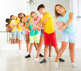 Wall Mural - Group of cheerful tween children standing in row one by one, learning movements of vigorous funny dance in choreography lesson.