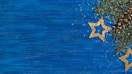 Wall Mural - christmas and new year festive background. fir branch with pine cone and wooden stars on blue rustic background. view from above.