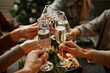 © Seventyfour - Close up of friends clinking champagne glasses while enjoying Christmas dinner together sitting by elegant dining table with candles