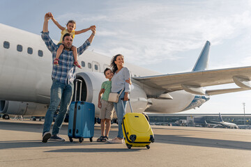 Man, woman and kids standing with suitcases with a big plane in the background