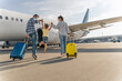 © Yaroslav Astakhov - Back view of parents holding the hands of the child and going with suitcases to board the plane