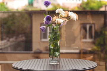 There is a beautiful bouquet in a vase on the dining table. The bouquet contains purple and white flowers.