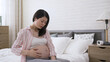 portrait asian woman in her last trimester is groaning and holding her belly while experiencing contraction pain by bedside in the bedroom.