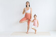 © Вадим Каштанов - Young woman practices yoga with her daughter. Children's yoga. Vrikshasana pose.