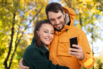 Poster - technology, season and people concept - happy couple with smartphone over autumn park background