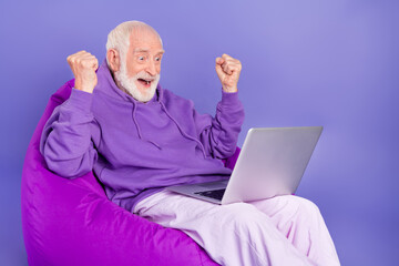 Portrait of handsome bearded elderly retired trendy lucky man pensioner using laptop rejoice isolated on vivid violet purple color background