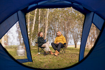 Canvas Print - camping, tourism and travel concept - happy couple cooking food in pot on tourist gas burner and talking at tent camp