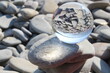 Glaskugel auf einem Steinstrand mit der Reflexion von Steinen und Wasser 