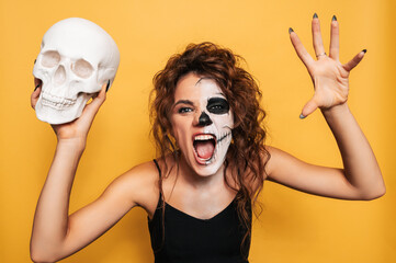Wall Mural - Studio shot of a girl in a costume of evil spirits at a Halloween costume party with a skull in her hands. The Art of Halloween