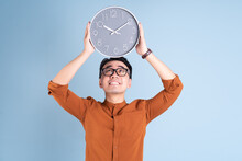 Young Asian Man Holding Clock On Blue Background