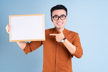 Wall Mural - Young Asian man holding white board on blue background