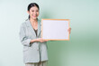 © Timeimage - Young Asian businesswoman holding white board on green background