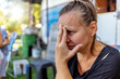 © Jelena Stanojkovic - Stressed depressed young mother sits outside in a playground with her kids playing behind her. Single frustrated woman hold her head with hands sitting on chair with playful kids on a background.
