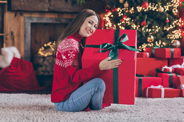 Wall Mural - Photo of pretty dreamy young woman dressed red sweater embracing new year big gift box smiling indoors room home house