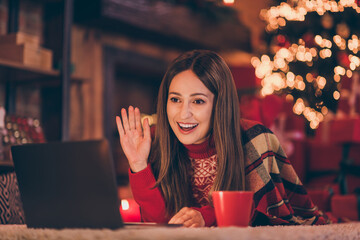 Wall Mural - Photo of cheerful pretty young woman dressed red sweater talking modern gadget sending new year greeting waving arm indoors room home house