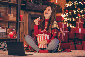 Wall Mural - Photo of pretty funny young woman dressed red sweater eating popcorn watching modern gadget new year film smiling indoors room home house