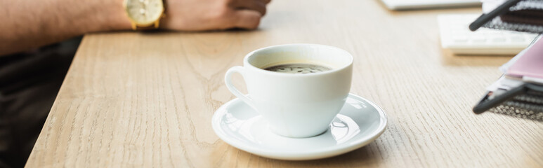 Wall Mural - Cropped view of cup of coffee near blurred businessman in office, banner