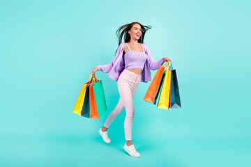 Sticker - Photo of adorable cute woman dressed purple clothes holding shopping bags walking looking empty space isolated teal color background