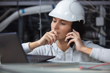 female technician in roof space using smartphone and studying laptop