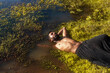 portrait of a dark skinned Indian man by a lake, shirtless, with make up, surrounded by nature