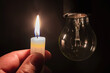 © Evgen - Burning candle near a switched off light bulb. Blackout, electricity off, energy crisis or power outage, concept image.