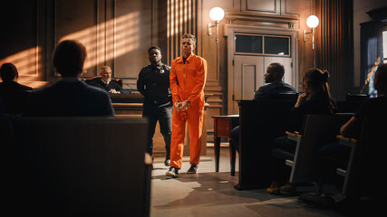 Cinematic Court of Law and Justice Trial Proceedings: Portrait of Accused Sad Male Criminal in Orange Jumpsuit Led Away by Security Guard in Front of Judge and Jury. Sentenced to Serve Jail Time.