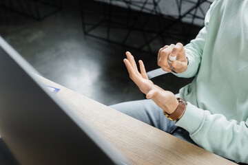 Wall Mural - Cropped view of businessman using hand sanitizer near blurred computer monitor in office