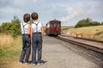 Wall Mural - Beautiful children, dressed in vintage clothes, enjoying old steam train on a hot summer day